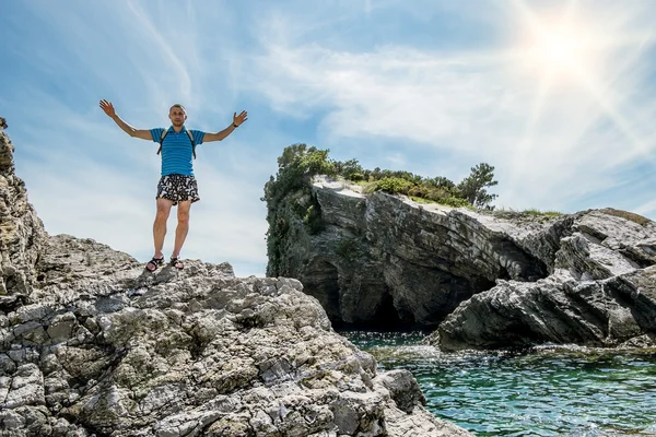 Man arms outstretched standing on a rock by the sea — Stock Photo, Image