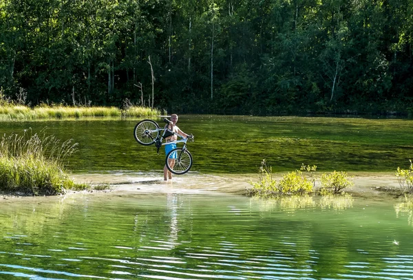 Rowerzysta, trzymając jego rower, stojąc w rzece — Zdjęcie stockowe