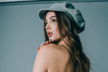 Göz kamaştırıcı genç kadın gri duvarda dalgalı saçlarıyla şık bir elbise giyiyor. Kahverengi saçlı güzel bir genç kız. Stüdyodaki siyah beyaz bir kızın portresi.