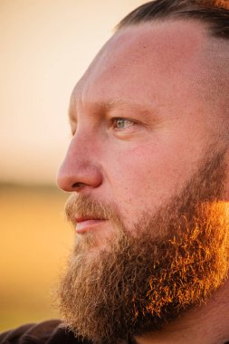 Hippi tarzı sakallı adam. Çekici adam, uzun saçlı, Avrupalı görünümlü, sakallı. Kahverengi tişörtlü adam.