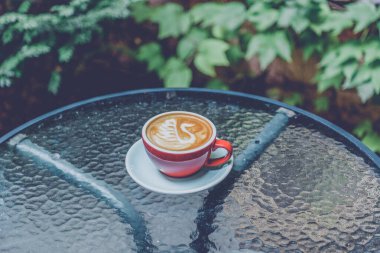 Kırmızı kahve fincanı. Bahçede kırmızı kahve fincanı. Kahveli latte, kırmızı bardakta. Kırmızı fincan latte sanatı. Sabah kahvesi.