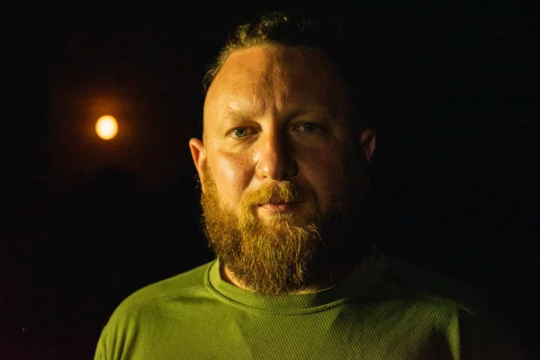 Hipster style bearded man. the attractive man the blonde with long hair of the European appearance with a beard. Man in green t-shirt. Night portrait of a man