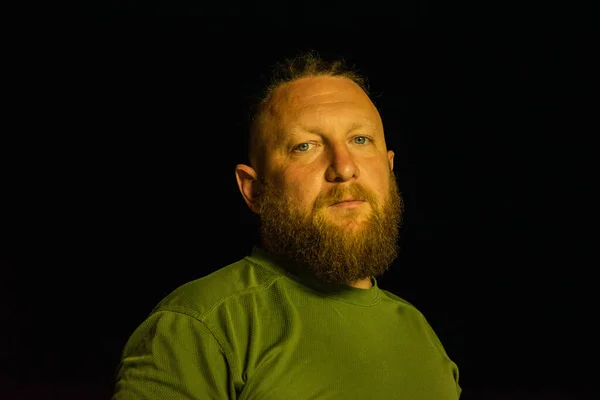Hipster style bearded man. the attractive man the blonde with long hair of the European appearance with a beard. Man in green t-shirt. Night portrait of a man