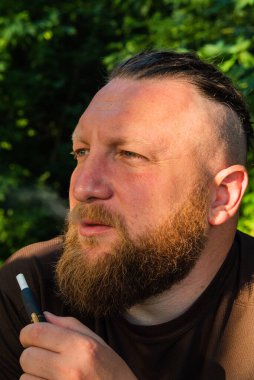 Yüzünde ciddi bir ifadeyle ağaca yaslanan bir adam profili. Ağaçta sakallı bir adamın profili. Ormanda sakallı yakışıklı bir adamın portresi.