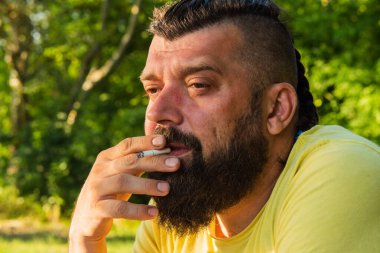 Hippi tarzı sakallı adam. Avrupa görünümlü uzun saçlı, sakallı çekici adam. Sarı tişörtlü adam. Adam sigara içiyor. Sigara içmek.