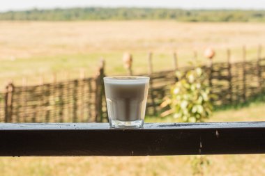 Ahşap masada, arka planda bir bardak süt. Bir bardak taze süt ahşap masada bulanık yeşil doğa ve sabah ışığı arka planında. Organik yiyecekler