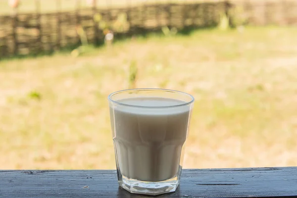 Glass of milk on wooden table, on field background. A Glass of fresh milk on wooden table with blurr green nature and morning light background. Organic food