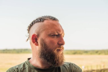 Yüzünde ciddi bir ifadeyle ağaca yaslanan bir adam profili. Ağaçta sakallı bir adamın profili. Ormanda sakallı yakışıklı bir adamın portresi.