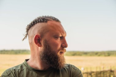 Yüzünde ciddi bir ifadeyle ağaca yaslanan bir adam profili. Ağaçta sakallı bir adamın profili. Ormanda sakallı yakışıklı bir adamın portresi.