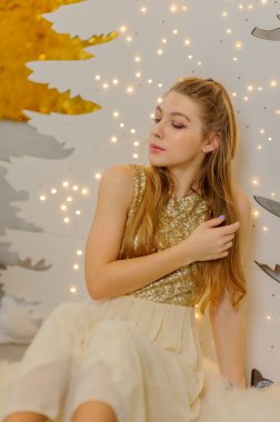 Noel, kış tatili konsepti. Noel için dekore edilmiş lüks dairelerde poz veren gece kıyafetli güzel bir kadın. Güzellik, moda. Noel için parlak elbiseli bir kız..