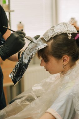 Kuaför, küçük şirin bir kıza saç stili yapıyor. Genç bir kızın kuaförde kakülleri hafifliyor. Turuncu kaküller. Parlak saç eğilimi.