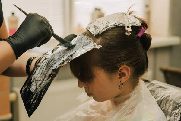 Hairdresser making a hair style to cute little girl. A teenage girl has her bangs lightened in a beauty salon. Orange bangs. The trend of bright hair.