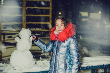 Karlı kış yürüyüşünde bir kardan adamla takılan mutlu kız çocuğu. Kız kardan adam yapıyordu. Noel sezonu. Yeni yıl. Kış. Genç bir kız kardan adam heykeli yapıyor.