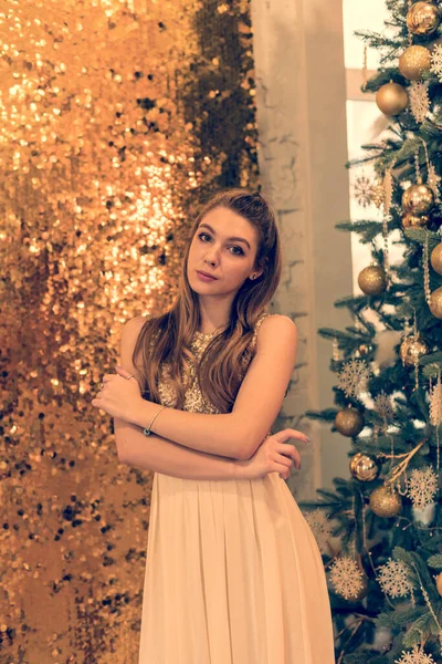 光沢のある夜のドレスの少女 少女は夢を見ている クリスマス 光と金の装飾が施されたファーツリーで居心地の良い休日 スタジオのクリスマスを背景にキラキラしたドレスを着た女の子 — ストック写真