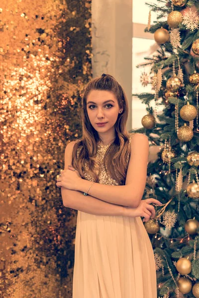 光沢のある夜のドレスの少女 少女は夢を見ている クリスマス 光と金の装飾が施されたファーツリーで居心地の良い休日 スタジオのクリスマスを背景にキラキラしたドレスを着た女の子 — ストック写真