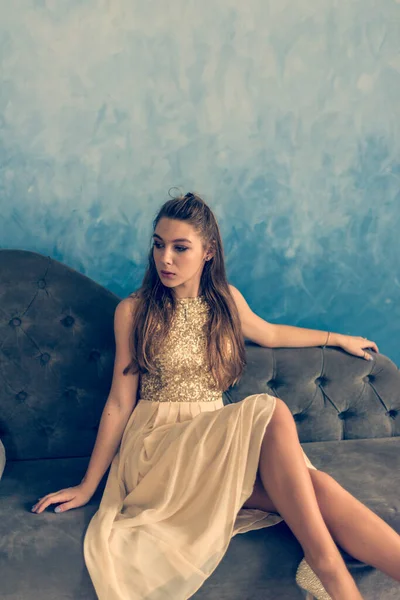 美丽的性感女人坐在沙发上的照片 一个穿着连衣裙的女孩正坐在沙发上 — 图库照片