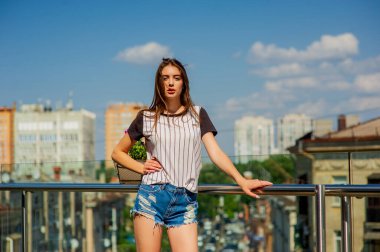 Balkonda kot şortlu bir kız. Balkonda poz veren genç hippi kızın yaz portresi.