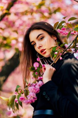 Uzun saçlı kız, çiçek açan sakura ağacının yanında bahar doğasının güzelliğinin tadını çıkarıyor..