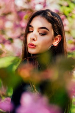 Uzun saçlı kız, çiçek açan sakura ağacının yanında bahar doğasının güzelliğinin tadını çıkarıyor..