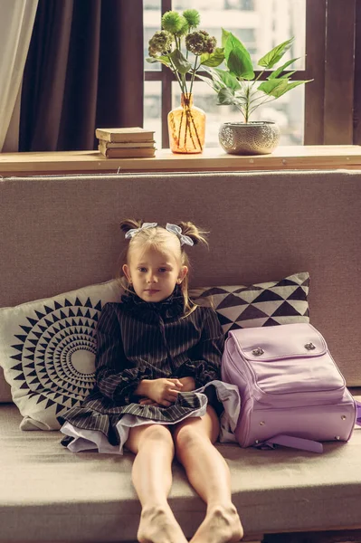 Schoolgirl in a school dress on a gray sofa. Back to school. Girl first grade