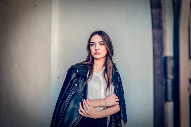 Siyah deri ceketli genç kız ayakta duruyor. Açık havada güzel bir esmerle çekilmiş bir dizi fotoğraf..
