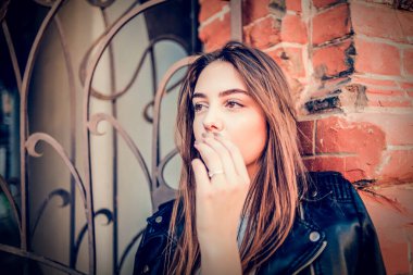 Siyah deri ceketli genç kız ayakta duruyor. Açık havada güzel bir esmerle çekilmiş bir dizi fotoğraf..