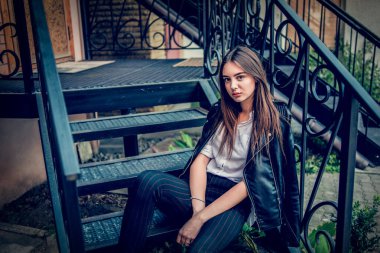 Siyah deri ceketli genç kız ayakta duruyor. Açık havada güzel bir esmerle çekilmiş bir dizi fotoğraf..