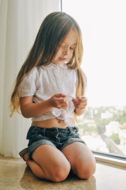 Neşeli çocuk portresi pencere kenarında durur. Pencere kenarında oturan küçük kız. Beyaz gömlekli çocuk.