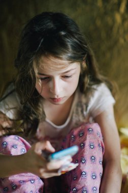 Pijamalı ergen kız telefona bakıyor. Yatağında akıllı telefonu olan genç bir kız.