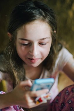 Pijamalı ergen kız telefona bakıyor. Yatağında akıllı telefonu olan genç bir kız.