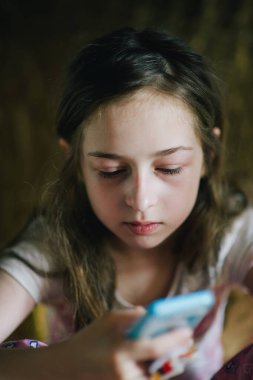 Pijamalı ergen kız telefona bakıyor. Yatağında akıllı telefonu olan genç bir kız.