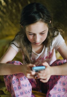 Pijamalı ergen kız telefona bakıyor. Yatağında akıllı telefonu olan genç bir kız.