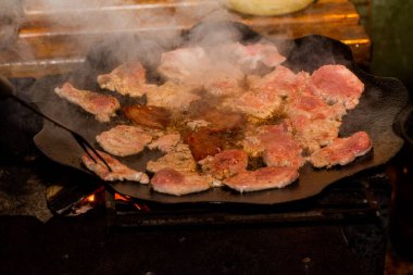 Kamp ateşinde pişen taze domuz pastırması. Et ateşte tavada kızarıyor.