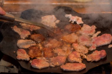 Kamp ateşinde pişen taze domuz pastırması. Et ateşte tavada kızarıyor.