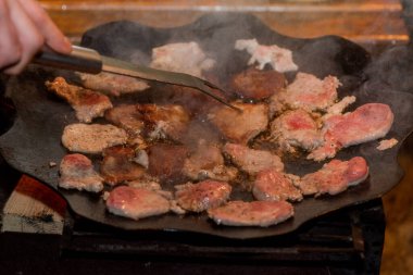 Kamp ateşinde pişen taze domuz pastırması. Et ateşte tavada kızarıyor.