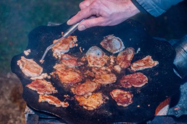 Kamp ateşinde pişen taze domuz pastırması. Et ateşte tavada kızarıyor.