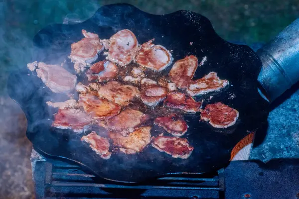 新鮮なカットベーコンはキャンプファイヤーの上で調理されています 肉は火の上の鍋で揚げられる — ストック写真