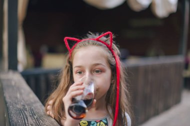 Lokantada içen sevimli, komik küçük kız. Kız bir yaz kafesinde bardaktan içiyor..