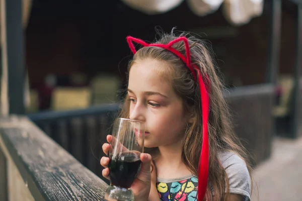 Charming Funny little girl drinks in a restaurant. Girl drinks from a glass in a summer street cafe.