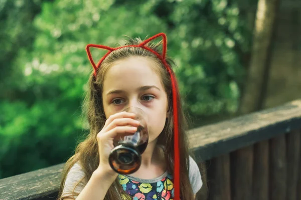 Charming Funny little girl drinks in a restaurant. Girl drinks from a glass in a summer street cafe.