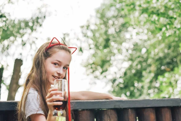 Charming Funny little girl drinks in a restaurant. Girl drinks from a glass in a summer street cafe.