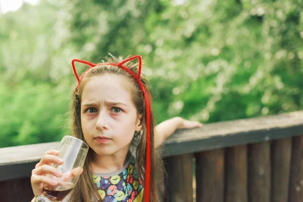 Charming Funny little girl drinks in a restaurant. Girl drinks from a glass in a summer street cafe.