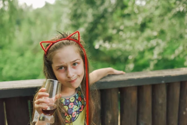 Charming Funny little girl drinks in a restaurant. Girl drinks from a glass in a summer street cafe.