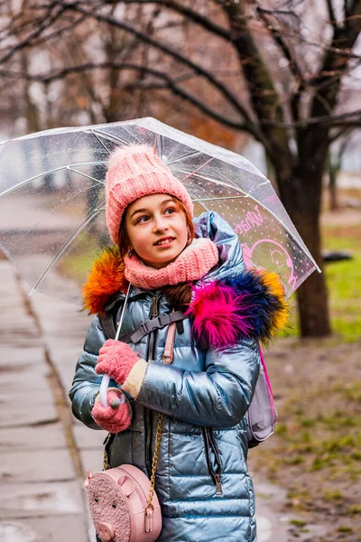 girl in a jacket with a transparent umbrella in the rain in the cold. Teenager under an umbrella
