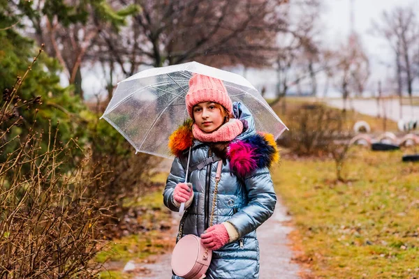 girl in a jacket with a transparent umbrella in the rain in the cold. Teenager under an umbrella