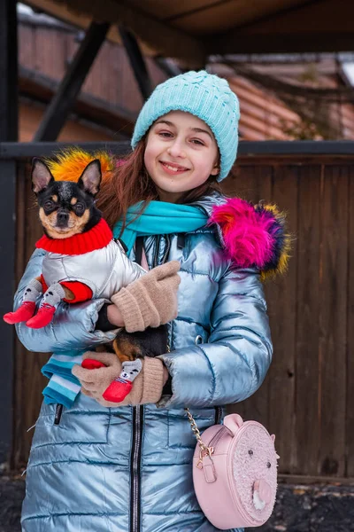 Girl and dog in winter outfits. Dog in clothes. Teenager smiling with a pet in her arms