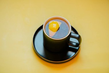 Limon çayı. Sarı arka planda limonlu siyah çay. Siyah bardakta bir dilim limonlu çay