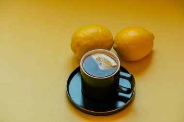 Çay. Çay, bir fincan siyah bardakta bir dilim limon ve bir fincan çay. Sarı arka planda iki limon