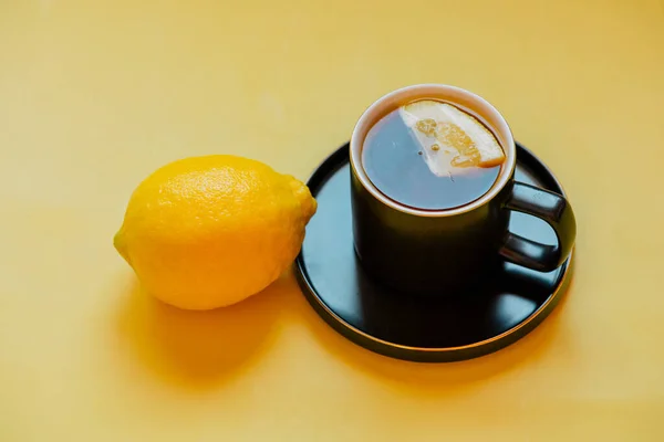 tea. Tea with a slice of lemon in a black cup on a saucer. lemon fruit on the yellow background