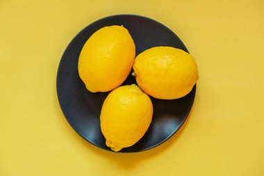Sarı arka planda siyah bir tabakta limonlar. Geçmişi. Turunçgil, meyve